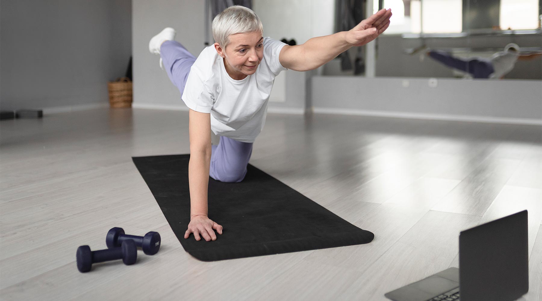 Persona mayor haciendo ejercicios de pilates  en el gimnasio sobre una colchoneta.