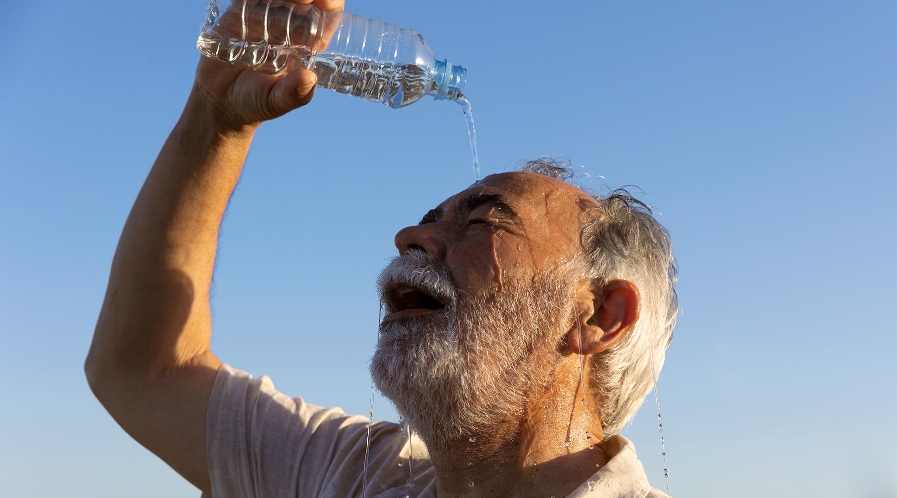 Anciano refrescándose con una botella de agua.