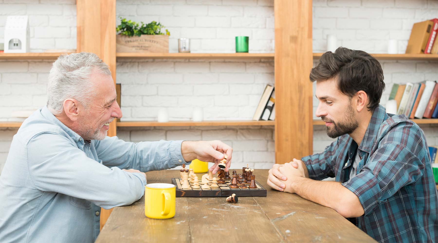 Persona mayor feliz y chico joven jugando al ajedrez en una mesa.